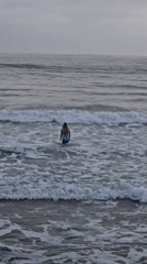 Woman stands in choppy ocean waters under overcast Oceanside sky