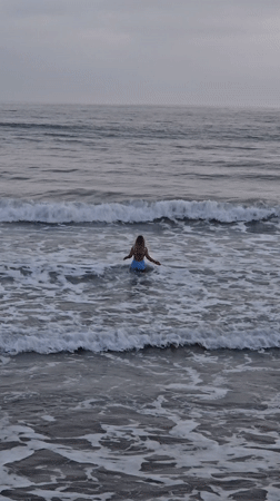 Woman stands in choppy ocean waters under overcast Oceanside sky