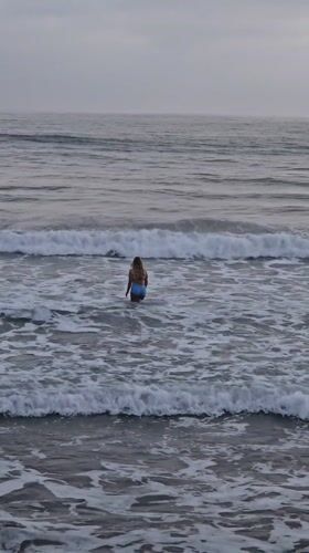 Woman stands in choppy ocean waters under overcast Oceanside sky