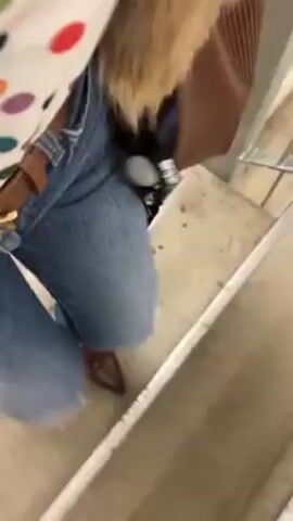 Here's a description of the video:

The video shows a person descending a set of concrete stairs. They are wearing ripped blue jeans, brown shoes and carrying a bag with a black and white lanyard hanging from it. The person's hair is blonde, and they are also wearing a brown jacket. The focus is on the person's legs and feet as they walk down the stairs.