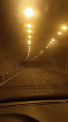 First-person drive through a tunnel lined with ceiling and green road lights.