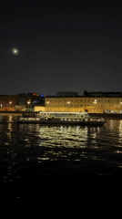 Night boat crosses river past illuminated city buildings