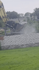 Excavator tears down a white brick wall, section by section