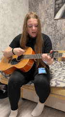Young woman plays acoustic guitar on bed in Chaikovsky