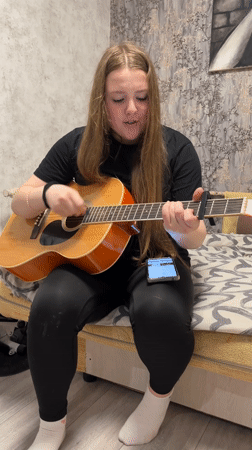 Young woman plays acoustic guitar on bed in Chaikovsky
