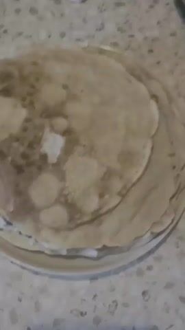 A stack of crepes sits on a white plate, which is on a speckled countertop. The crepes are light brown with darker brown spots and appear to be thin and layered.