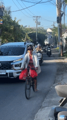 Cyclist with red bags rides narrow North Kuta street