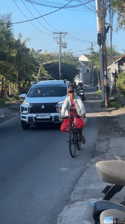Cyclist with red bags rides narrow North Kuta street