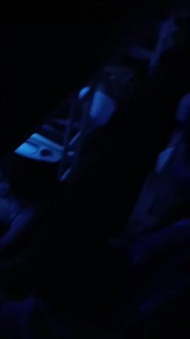The video is a shaky, dark, first-person perspective recording of the interior of a bus at night. Blue LED lights illuminate the aisle and overhead compartments. The seats are dark and appear to be empty or occupied by figures obscured by the darkness. The camera moves slowly, capturing glimpses of the bus's interior, including some luggage and what appear to be personal electronic devices. The overall atmosphere is dim and somewhat unsettling due to the low light and movement.