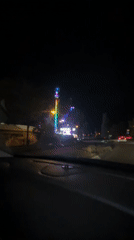 Colorful pendulum tower ride spotted from a passing vehicle at night
