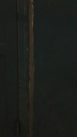 The video shows a close-up of a dark green door. The door is closed and appears to be made of metal. There is a gap between the door and the frame, and some light is visible through the gap. The image is slightly blurry, and the lighting is dim.