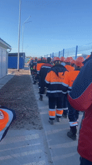 Workers in hard hats walk single file in Koskolovo