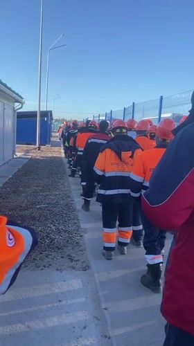Workers in hard hats walk single file in Koskolovo