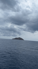 Boat crossing overcast Indonesian waters toward a rocky island