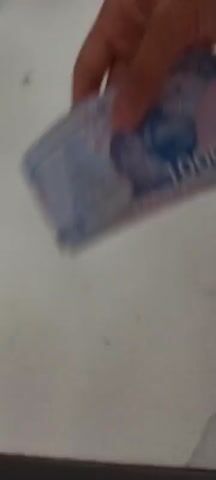 A hand is shown holding and then fanning out a stack of Uzbekistan 10000 som banknotes. The banknotes are predominantly blue and white with pink accents. The denomination "10000" is visible on each banknote. The background appears to be a light-colored, flat surface, possibly a table. The action is performed on a white surface.