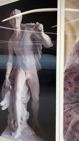 This video shows a series of superimposed images of classical statues in a retail display. The first statue, a male figure, is wearing a denim shirt and orange shorts. The second image is a close-up of a female statue partially obscured by a floral pattern. The third image shows a female statue with her arm raised. The display appears to be in a store window or a similar commercial setting.