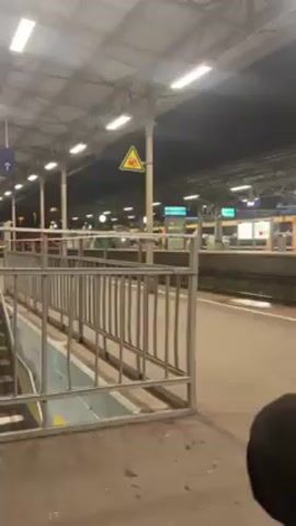 The video shows a train station platform at night. The platform is empty, with a staircase leading down to another level. There are signs indicating the direction of platforms 6-7. The lighting is bright, and the scene is quiet.