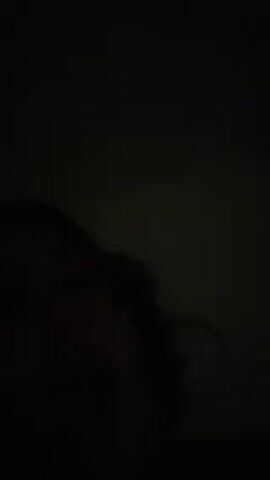 A person with dark hair is visible in a very dimly lit, dark room. Their features are barely discernible.