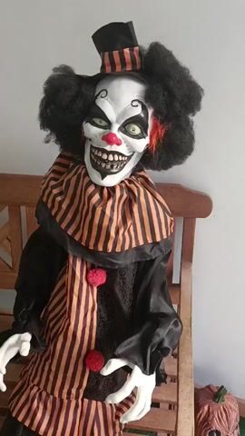 The video shows a scary clown doll on a wooden bench, then a scary butler doll holding a silver tray with papers on a wooden bench, then the view looking through a glass door into a room with wood floors and a receptionist inside, where there is a Push To Ring bell.