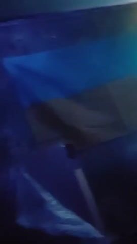 The video shows a dimly lit room with colored lights. In the first few seconds, a keyboard with RGB lighting is visible. Later, a projector casts a swirling blue and green light pattern on the wall. Finally, a neon sign that appears to say "ДОНЕЦЬКА ОБЛАСТЬ" in Ukrainian, illuminated with pink and cyan lights, is shown. There are no people visible in the video.