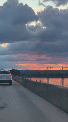 Evening car journey captures dramatic sunset over water near Chaikovsky