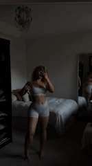 Woman takes mirror selfies in white athletic wear, London bedroom