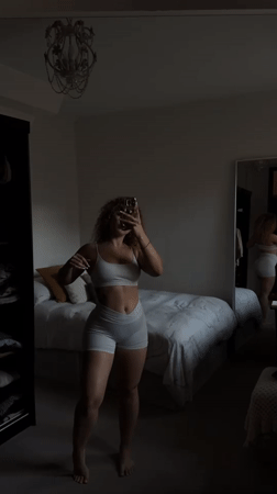 Woman takes mirror selfies in white athletic wear, London bedroom