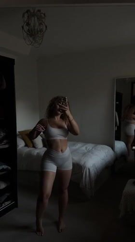 Woman takes mirror selfies in white athletic wear, London bedroom
