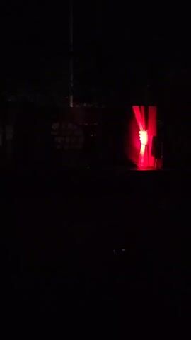 A person is dancing on a stage in front of a red curtain and a screen with bright lights. The audience is sitting in chairs in the dark. The video also shows a close-up of a red lamp with a bright light inside of it.