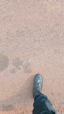 A person wearing black boots and black pants is walking on a rough, textured, brown and tan surface. The camera is pointed down at the person's feet as they move. A buzzing sound can be heard.