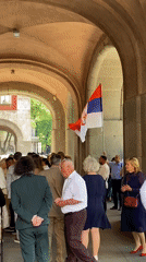 Crowd gathers with Serbian flag under stone archway in Subotica