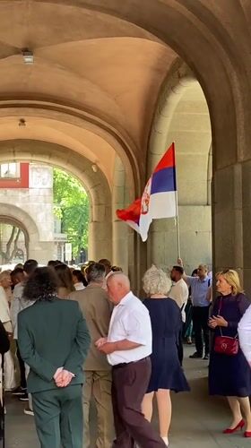 Crowd gathers with Serbian flag under stone archway in Subotica