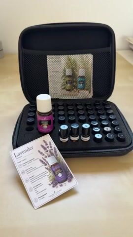 Here is a description of the video:

The video shows a black zipper case, opened to reveal a foam insert with many circular cutouts, a few of which contain small bottles of essential oil. There is also one larger bottle of "Young Living LAVENDER LAvande" essential oil standing up in one of the cutouts. Next to the case, there's a card with information about lavender essential oil, including an image of a bottle of it. The background appears to be a light-colored wooden table.