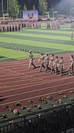 Mass uniformed formation on floodlit Chongqing sports field at night