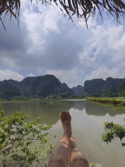 Person relaxes lakeside under thatched roof in Vietnam's Hoa Lư