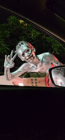 Silver-painted person gestures with box near car in Denpasar