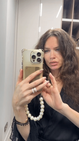 Woman applies makeup using phone camera in Khimki bedroom