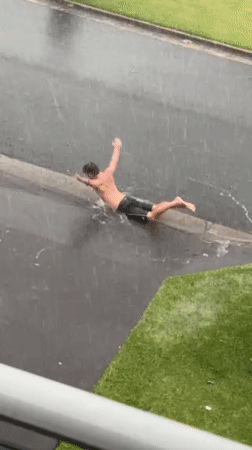 Person swims in flooded streets during heavy rainfall in Bulli