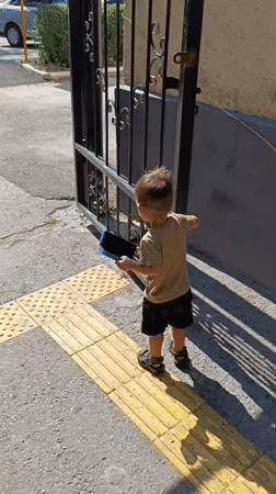 Kid explores a Taraz parking lot, climbing gates and checking cars