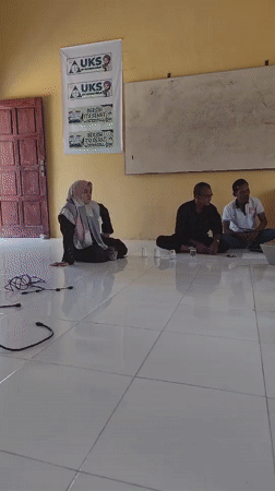 Six people gathered on a classroom floor, posters on yellow walls