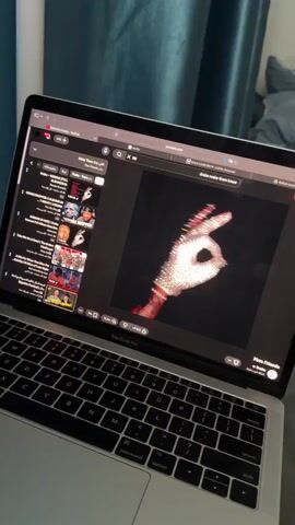 Here's a description of the video:

The video starts with a close-up shot of a silver MacBook Pro laptop playing music on YouTube. The song playing is "Make Them Cry" by Drake. The camera then pans upwards to show a view from a window.  White bars of the window frame are visible, along with a light blue curtain. The view outside is of a city with tall buildings and green trees under a clear blue sky.