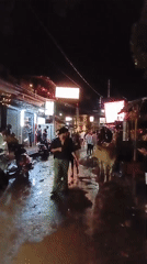 Evening street scene shows pedestrians, scooters, cow in Chapora