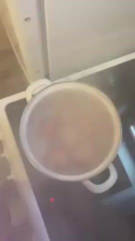 The video shows an overhead shot of a white pot on a stove. The pot is full of water that is boiling. There appears to be something submerged in the water, but it is hard to see due to the steam.