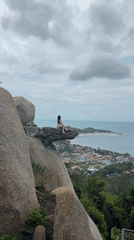 Woman sits on cliff rock formation in Thailand