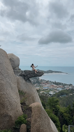 Woman sits on cliff rock formation in Thailand