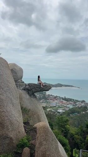 Woman sits on cliff rock formation in Thailand