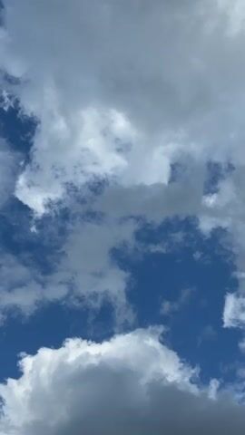 This is a vertical video of a cloudy sky. The clouds are white and grey, and the sky is blue. The clouds are moving slowly.