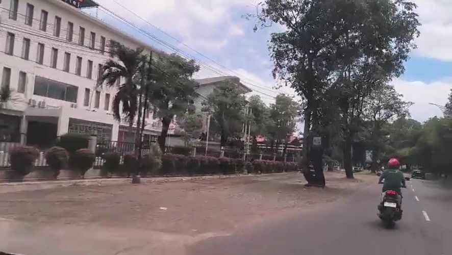 Motorcyclist travels tree-lined road in Banda Aceh morning