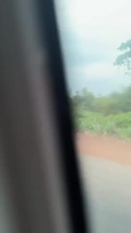 The video shows a truck driving on a road. The truck is loaded with a large quantity of green bananas. The truck has "God's Grace And Mercy" written on its side. The road is next to a patch of green trees and bushes. The sky is cloudy. The camera appears to be mounted inside a vehicle, possibly another car. The scene is shot from a low angle.