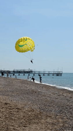 Parasailer glides over calm Turkish coast beneath yellow cartoon parachute